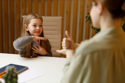 Sign language, smiling deaf-mute little girl communicates with her mother at the table.